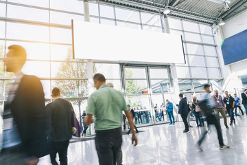 Crowd of anonymous people walking at a trade show, with banner for copy space