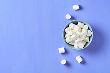 Full gray ceramic bowl of sugary white marshmallow cylindrical form on purple scratched concrete table. Space for text. Top view