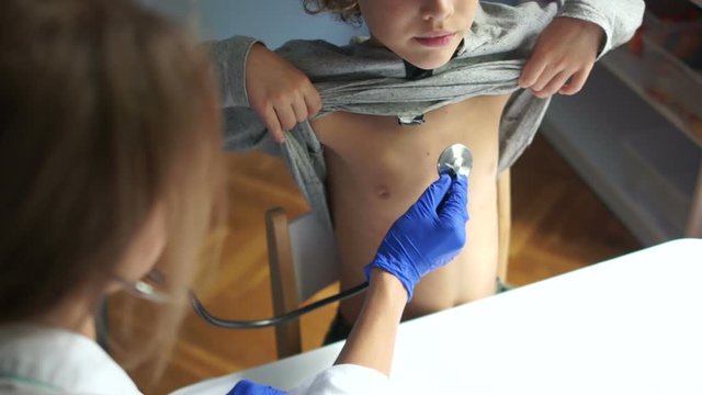 Pretty doctor examines a young boy patient listening with phonendoscope. International Doctors Day, Pediatrics