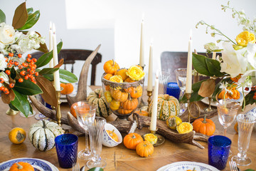 Luxurious elegant wedding decor in autumn style. Wooden vintage table setting with ceramic plates and silver cutlery. Fresh flowers in a vase, orange pumpkins, deer horns and candles. Romantic dinner.