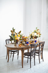 Luxurious elegant wedding decor in autumn style. Wooden vintage table and chairs setting with ceramic plates and silver cutlery. Fresh flowers in a vase, orange pumpkins, deer horns and candles.