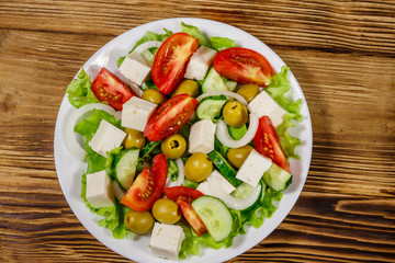 Greek salad with fresh vegetables, feta cheese and green olives on wooden table. Top view