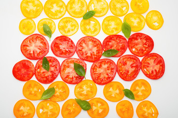 slices of ripe red, yellow and orange tomatoes decorated green leaves of basil on white background, flat lay