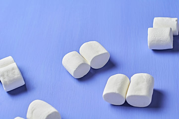 Lot of scattered double white marshmallows cylindrical form lies on purple scratched concrete table. Space for text