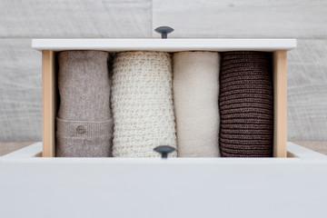 warm knitted women's clothing in brown, white and beige colors in the drawer of the chest of...