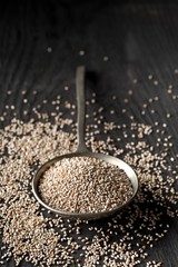 White whole, organic chia seeds heap in silver metal spoon on black rustic table background with...