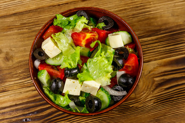 Greek salad with fresh vegetables, feta cheese and black olives on wooden table. Top view