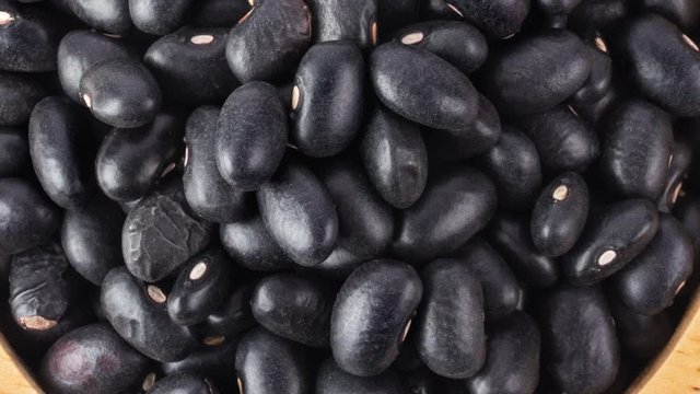 panning black beans in wood bowl isolated on white background. top view