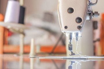 Close-up needle of white industrial sewing machine with blurred background and bokeh.