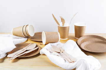 Fototapeta na wymiar Brown paper cups, plates, wooden cutlery, linen napkins on wooden background. Recycling concept.