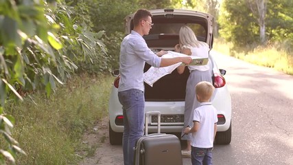 A young family with a small child travels by car, dad opens the map to see the route. Father and son look at the map during a summer trip.
