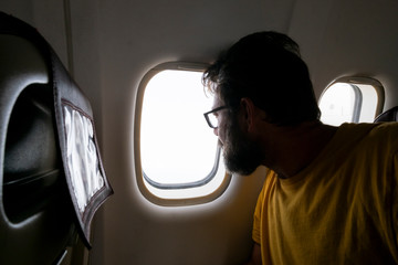 Bearded traveler man look outside the window inside the aiplane flying and traveling - tourism and vacation rtip concept with adult people and flights