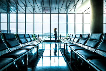 Young woman tourist people walking at the airport mirrored on the clean floor and looking outside the window to the filghts start and arrive - delay and canceled at the gate concept