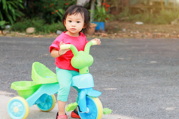 Happy Asian child girl playing and practice to ride a bike on the road at the playground park. She smiling and laughing. 