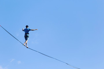 A man is walking along a stretched sling. Highline in the mountains. Man catches balance....
