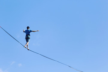 A man is walking along a stretched sling. Highline in the mountains. Man catches balance. Performance of a tightrope walker in nature. Highliner on the background of the mountains.