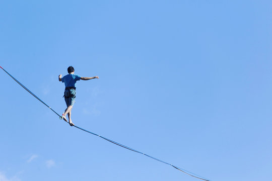 A man is walking along a stretched sling. Highline in the mountains. Man catches balance. Performance of a tightrope walker in nature. Highliner on the background of the mountains.