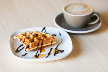 Plate of belgian waffles  and cup of coffee and on light wooden table