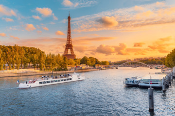 The main attraction of Paris and all of Europe is the Eiffel tower in the rays of the setting sun on the bank of Seine river with cruise tourist ships - obrazy, fototapety, plakaty