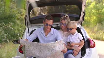 Close-up of young parents and a small five-year-old boy traveling by car, dad holding a map. A family in a car on an empty road in the woods studying a route map.