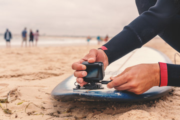 Male surfer attaches an action camera to a surfboard, sport and entertainment concept