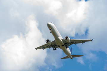 The plane is landing against the sky with clouds. Landing gear