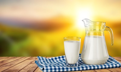 A glass of milk and a milk jug on plaid tablecloth