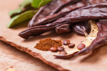 Carob. Organic carob pods with seeds and leaves on tree bark table. Healthy eating, food background.