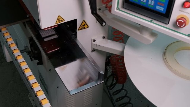 A modern machine with a control panel and a monitor for edging chipboard parts. Close-up of male hands. The white edge is glued to the brown blank. Real sound industrial noise in furniture production.