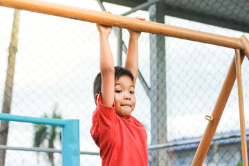 Obraz premium Kid exercise for health and sport concept. Happy Asian child boy playing and hanging from a steel bar at the playground. 5 years old.