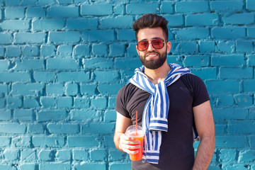 Handsome cheerful young arabian student with a stylish mustache and a beard with juice in his hands, walking around the city after a working day. Concept of positive and rest.