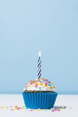 Birthday cupcake with candle on blue background