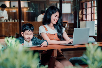 Mother and son using laptop computer and digital tablet in tea cafe. Happy family time.