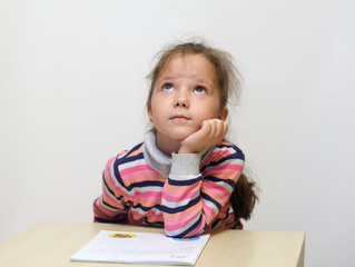 Naklejka premium The adorable little girl doing homework and dreams.