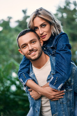 Young beautiful lovers have fun on nature. Smiling girl piggyback of her boyfriend