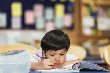 An image of Asian school boy with a pencil in right hand writes his practice seriously in a classroom. Young student intent on studying. Boy concentrated in the study. 