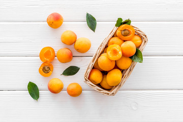 Fresh raw apricots in basket on white wooden background top view pattern with leaves