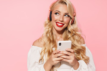 Image closeup of charming seductive woman wearing red lipstick listening to music with wireless headphones and cellphone