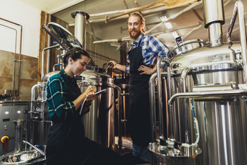 Women with clipboard working at brewery or beer plant. Brewery worker opening a lid of a beer cask at a craft beer brewery. Small business concept.