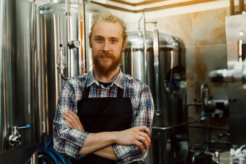 A portrait of handsome brewer with dreadlocks in uniform at the beer manufacture with metal...
