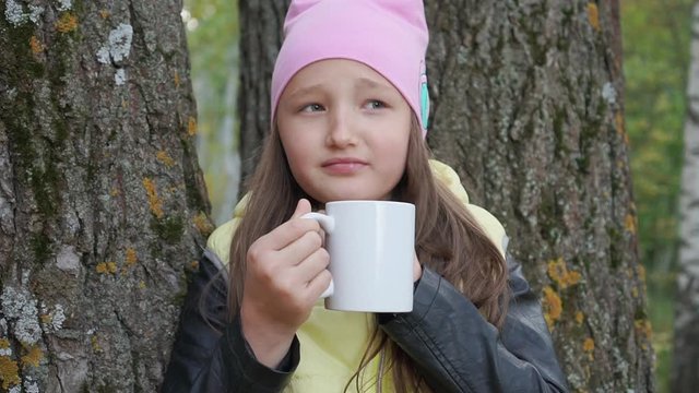 Little teenager girl drinks hot tea and it hurts, sore throat in the autumn forest. Sick little girl.