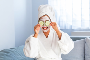 Woman with facial mask and cucumber slices in her hands. Beautiful young woman with facial mask on her face holding slices of fresh cucumber. Young woman with clay facial mask holding cucumber slices