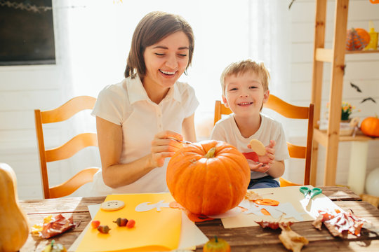 Happy Halloween. Young woman with her little son are preparing to Halloween on kitchen. Mother with son are having fun with pumpkins. Happy Halloween concept