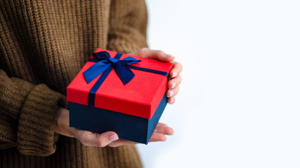 Woman in brown sweater holding gift box with blue ribbon in hands on white background