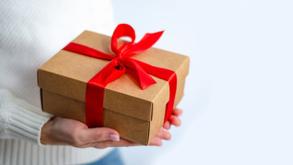 Woman in white sweater holding gift box with red ribbon in hands on white background
