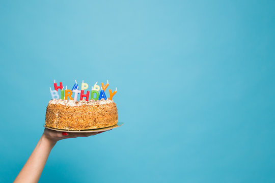 Hands holding a birthday cake with candles and the inscription birthday on a blue background. Copy Space
