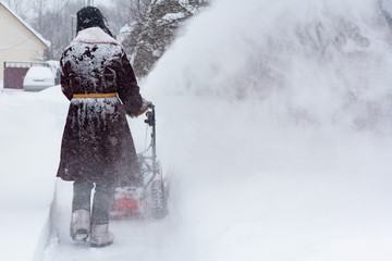 A man in sheepskin coat clears a snowdrift with a snow blower