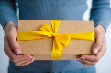 Woman in blue sweater holding gift box with yellow ribbon in hands on white background
