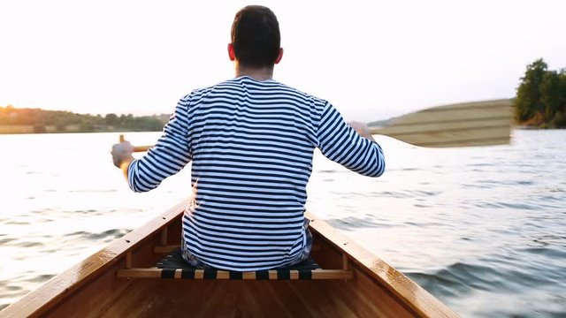 Man in sailor shirt paddling canoe on the sunset lake