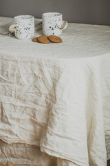 Two white cups on a linen tablecloth with oatmeal cookies. Rustic background